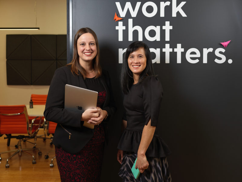 Amanda Newbery and Alice Sherring from Articulous Academy, standing in front of a grey wall with a decal that says 'work that matters'