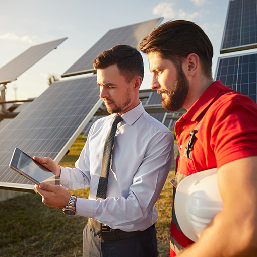 Focused male supervisor sharing tablet with technician near solar panels