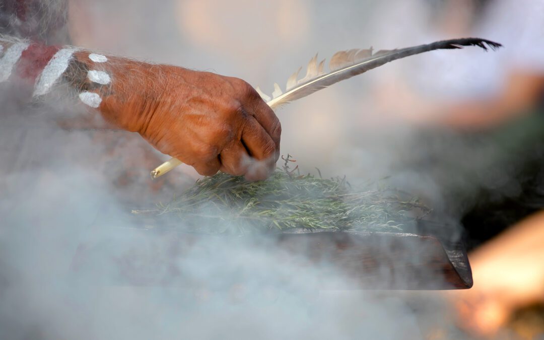 Human hand holding a wooden dish and feather at the smoke ritual rite at a indigenous community event in Australia.